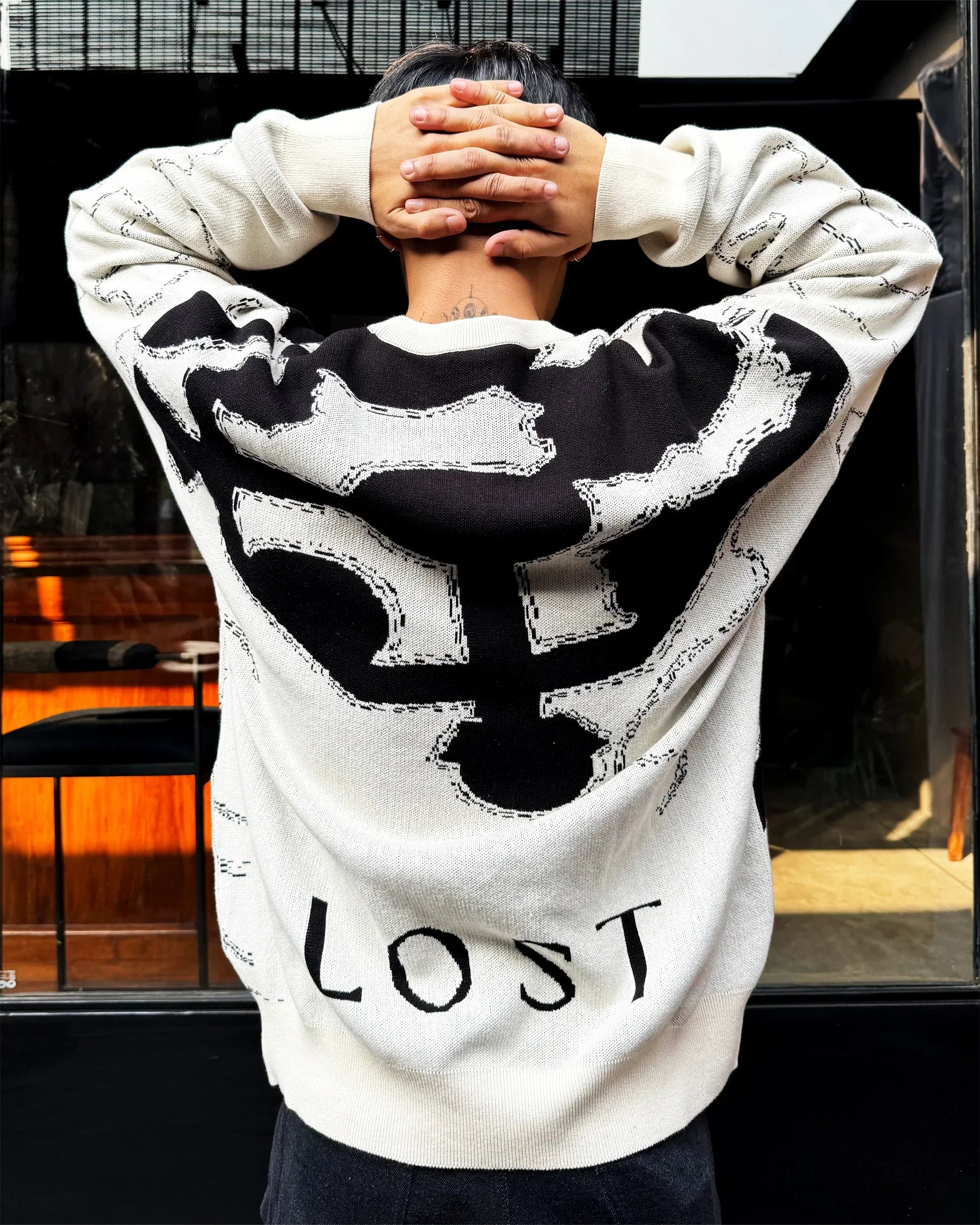 Person wearing white and black sweater with bone print and word LOST on back, posing indoors