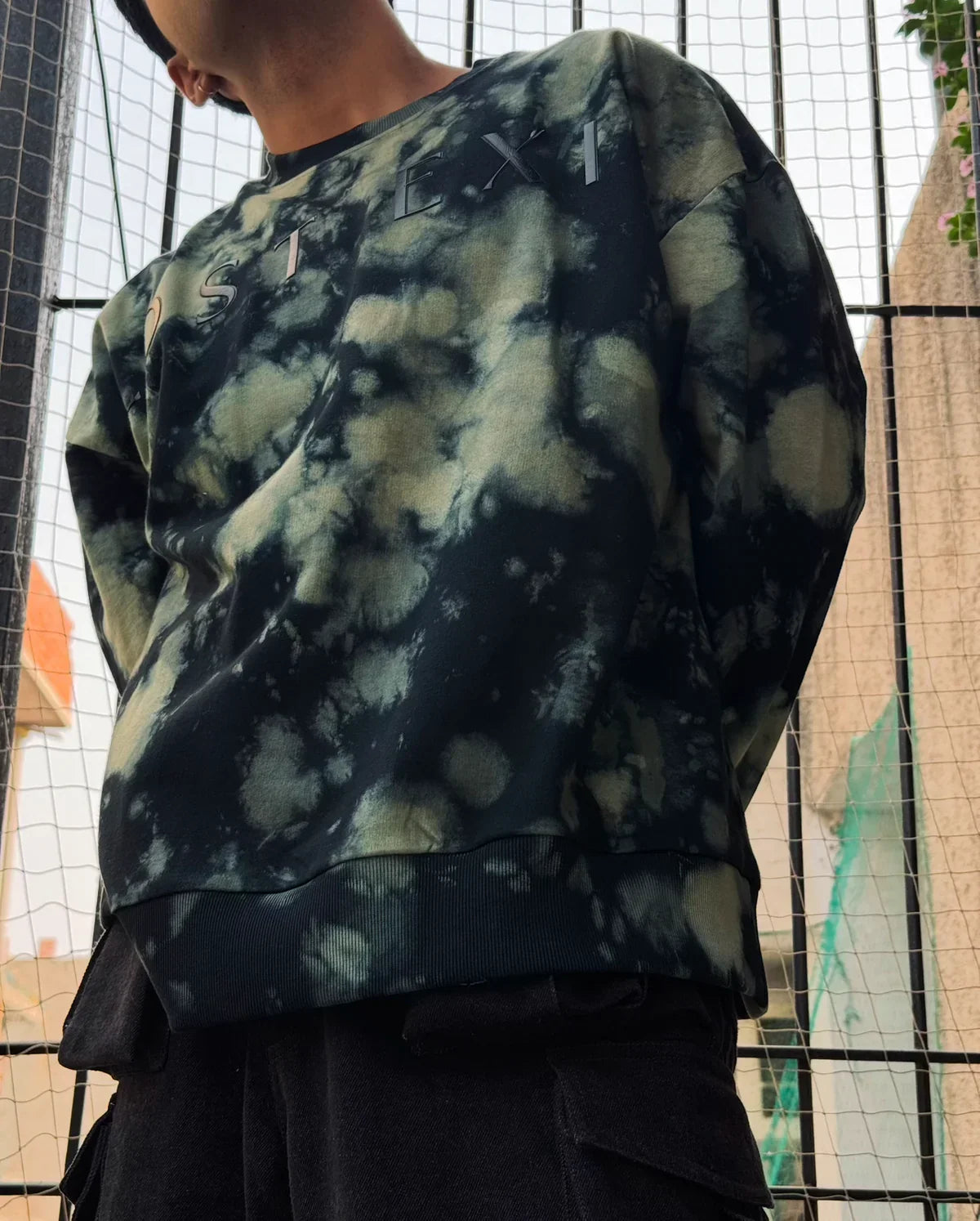 Person wearing black and green tie-dye Nike sweatshirt with visible logo and black cargo pants outdoors