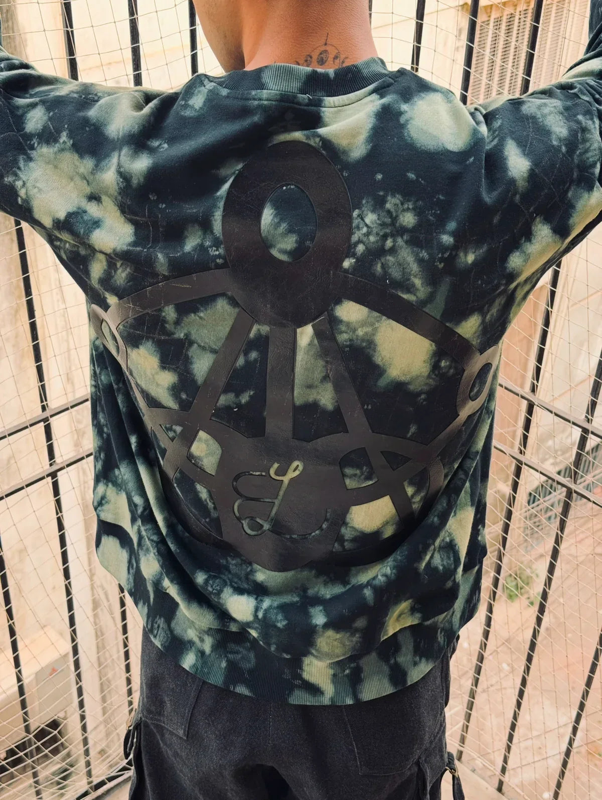 Person wearing black and green tie-dye sweatshirt with large black geometric design on the back