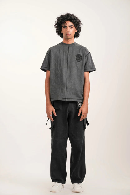Young man standing in studio wearing gray embroidered t-shirt, black cargo pants, and white sneakers