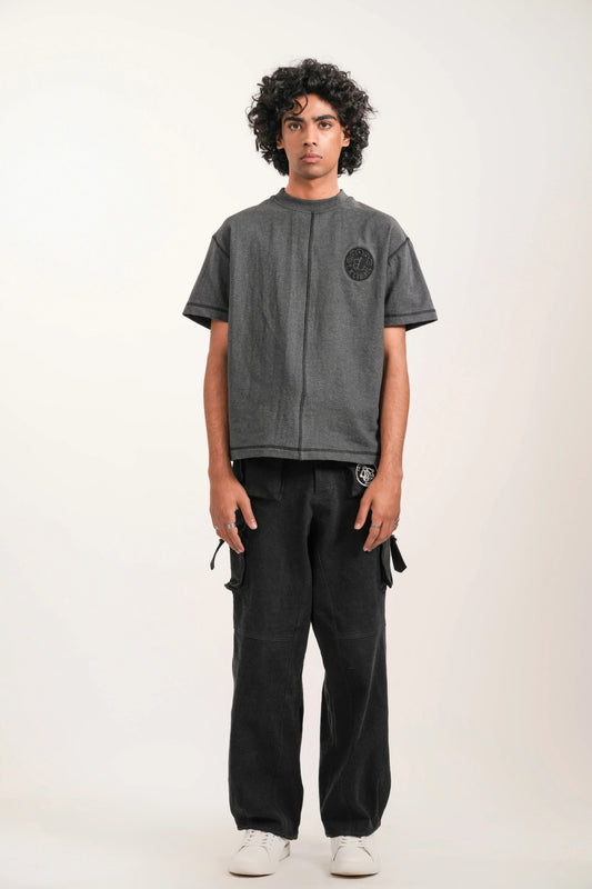 Young man standing in studio wearing gray embroidered t-shirt, black cargo pants, and white sneakers