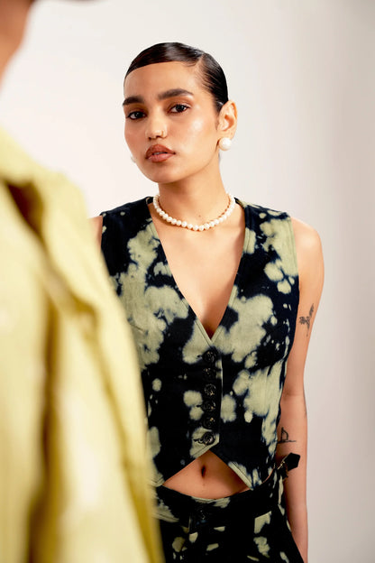 Young woman with sleek hair wearing black and green tie-dye vest and pearl necklace in studio