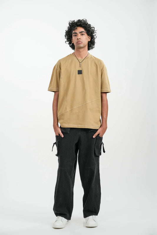 man wearing tan oversized t-shirt and black cargo pants with white sneakers standing against white background