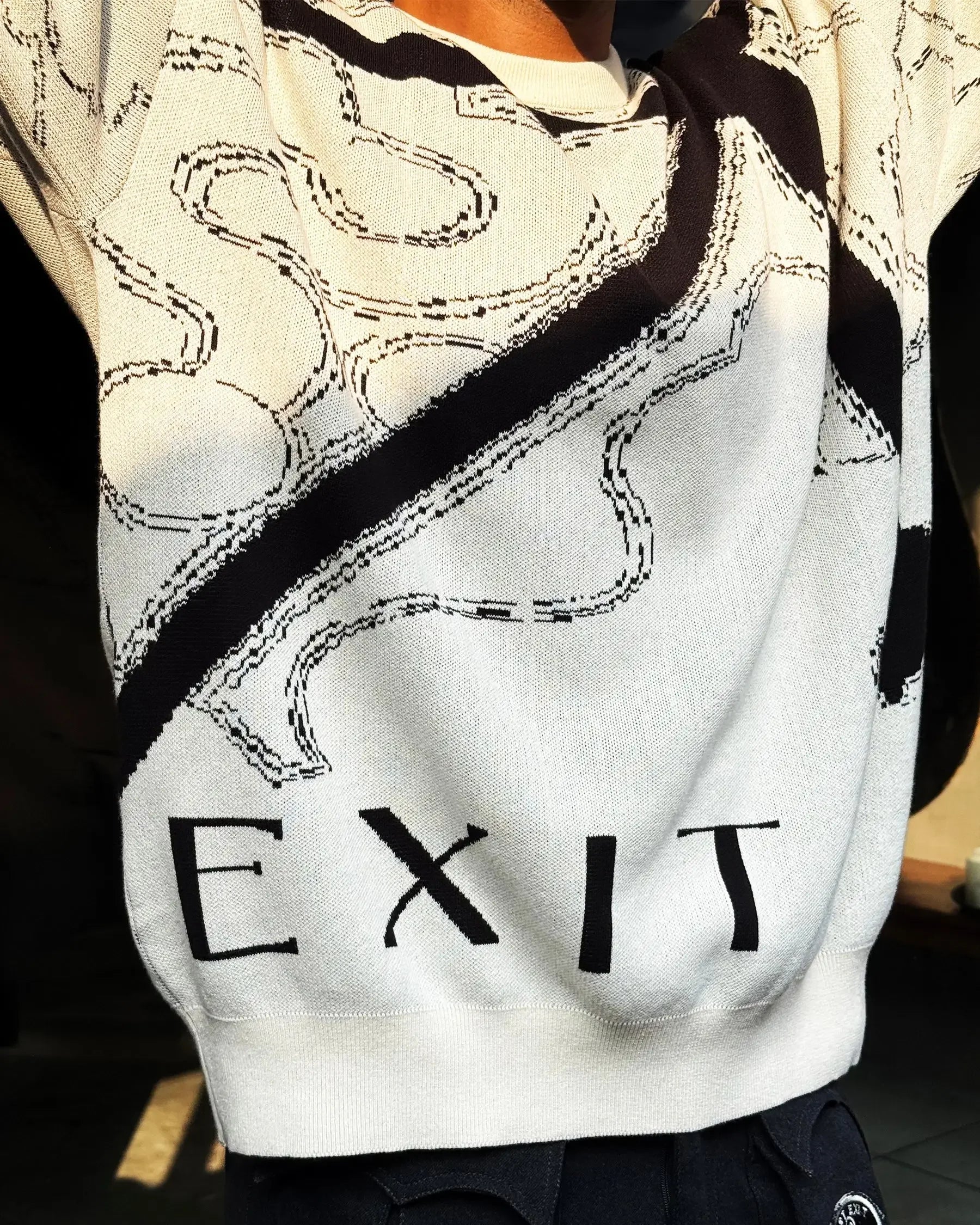 Close-up of person wearing white sweater with abstract black design and the word EXIT printed on it
